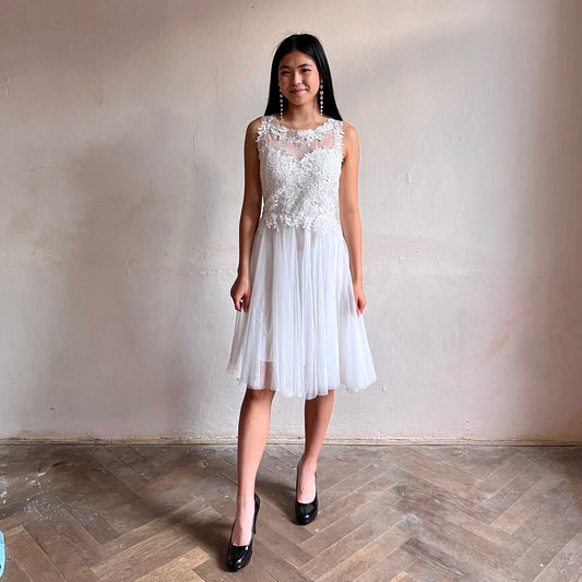 Modelka asijského původu pózující zepředu oblečená ve krátkých bílých společenských šatech 