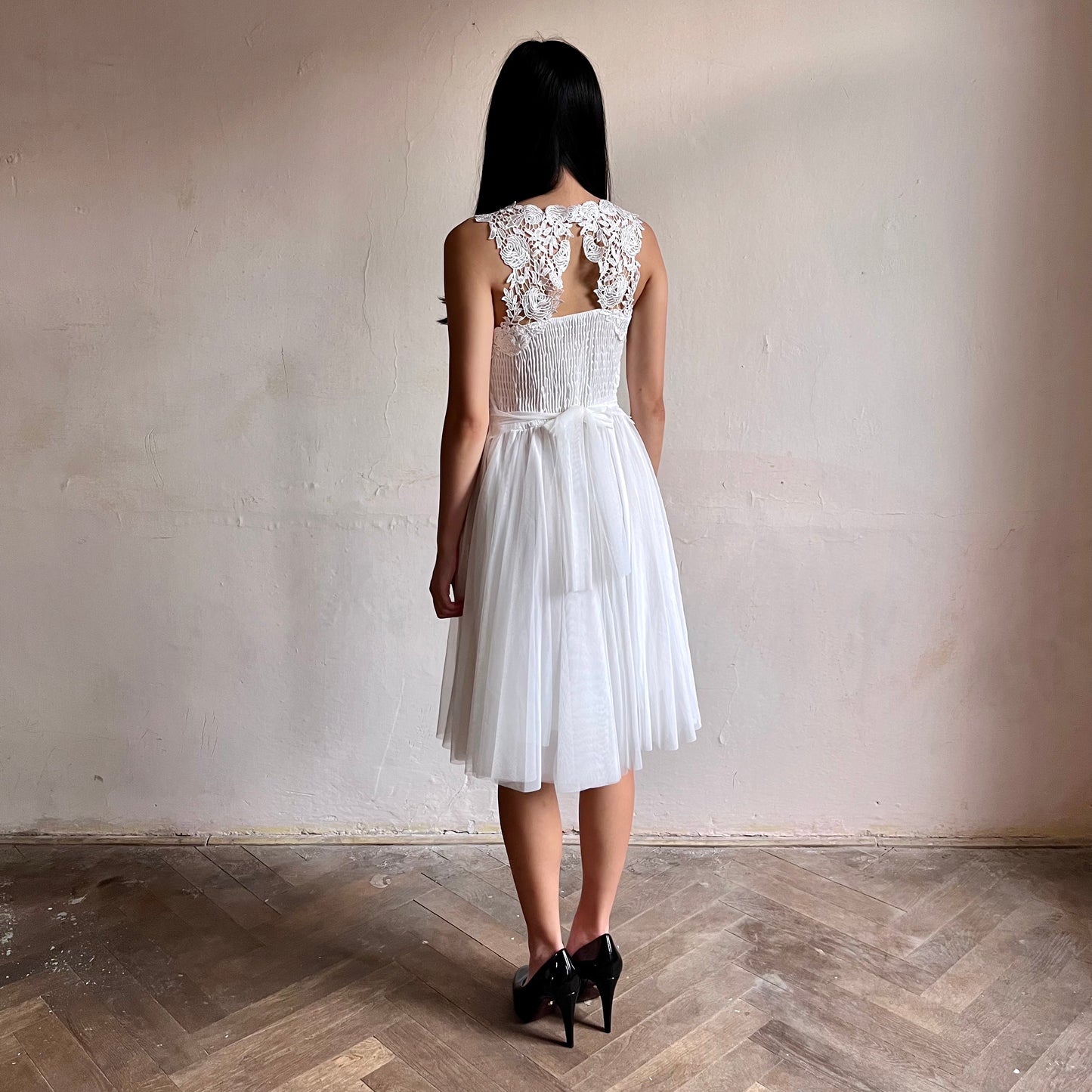 Modelka asijského původu pózující zezadu oblečená ve krátkých bílých společenských šatech 