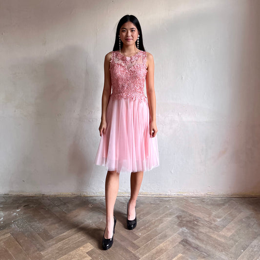 Modelka asijského původu pózující zepředu oblečená ve krátkých světle růžových společenských šatech 