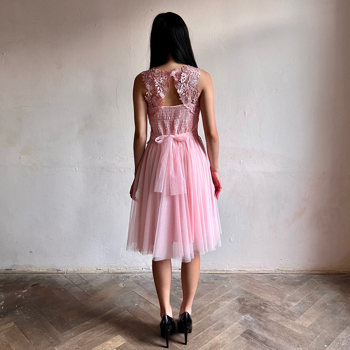 Modelka asijského původu pózující zezadu oblečená ve krátkých světle růžových společenských šatech 