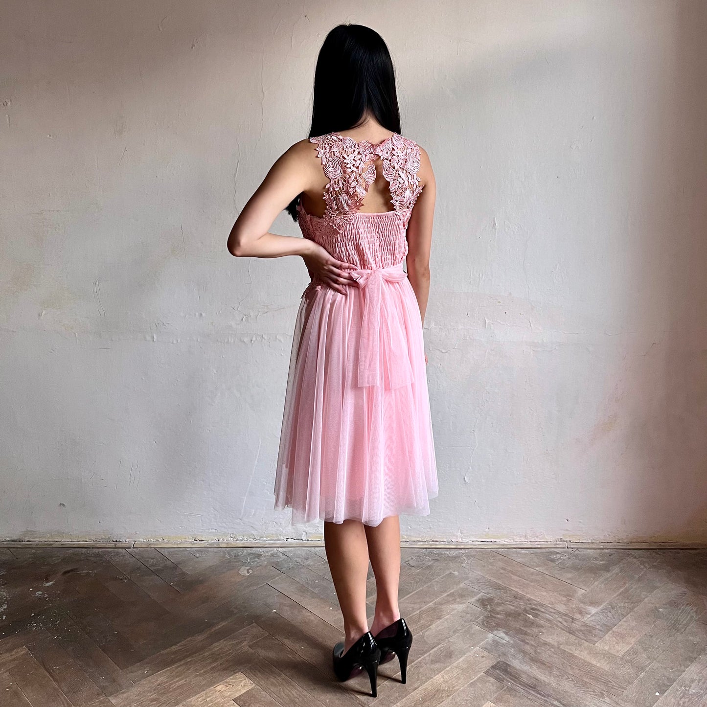 Modelka asijského původu pózující z boku oblečená ve krátkých světle růžových společenských šatech 