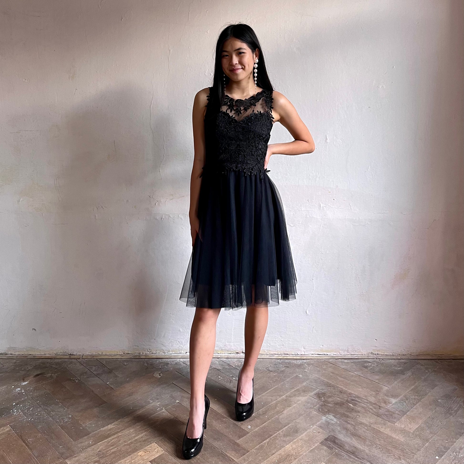 Modelka asijského původu pózující zepředu oblečená ve krátkých černých společenských šatech 