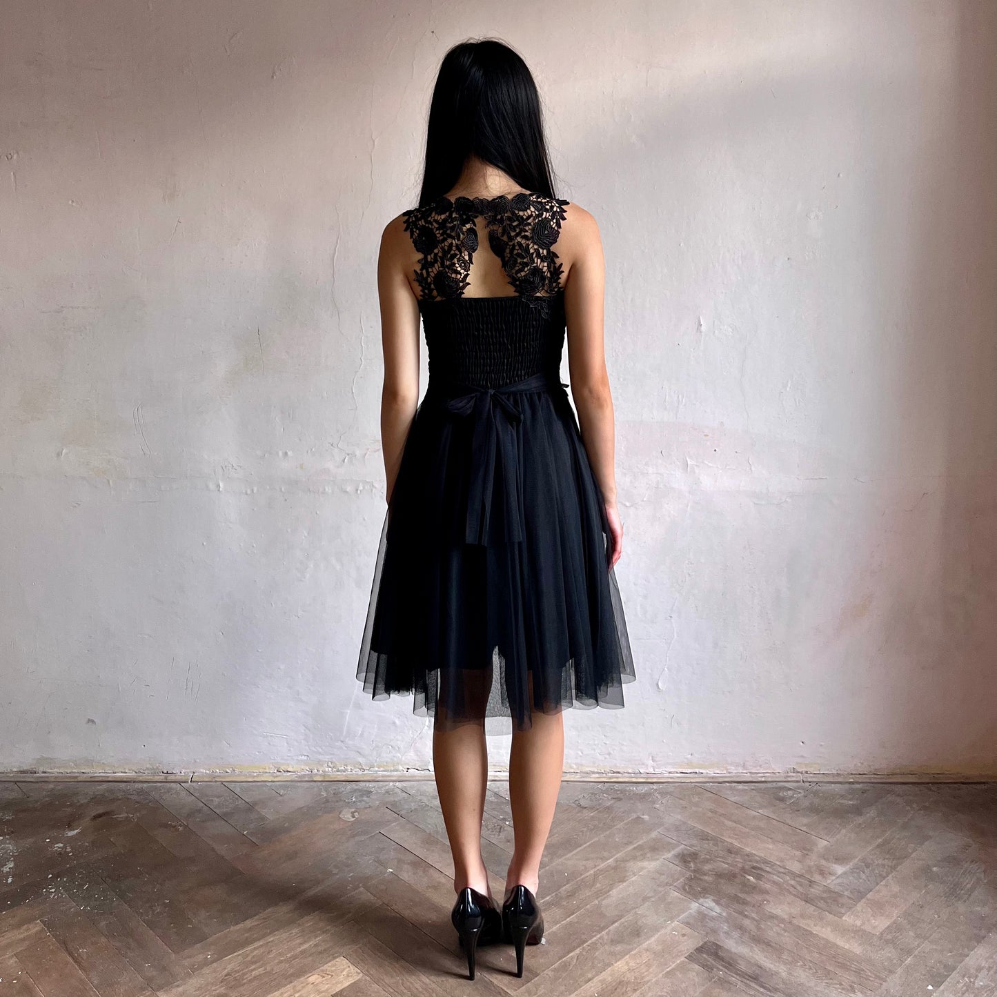 Modelka asijského původu pózující zezadu oblečená ve krátkých černých společenských šatech 