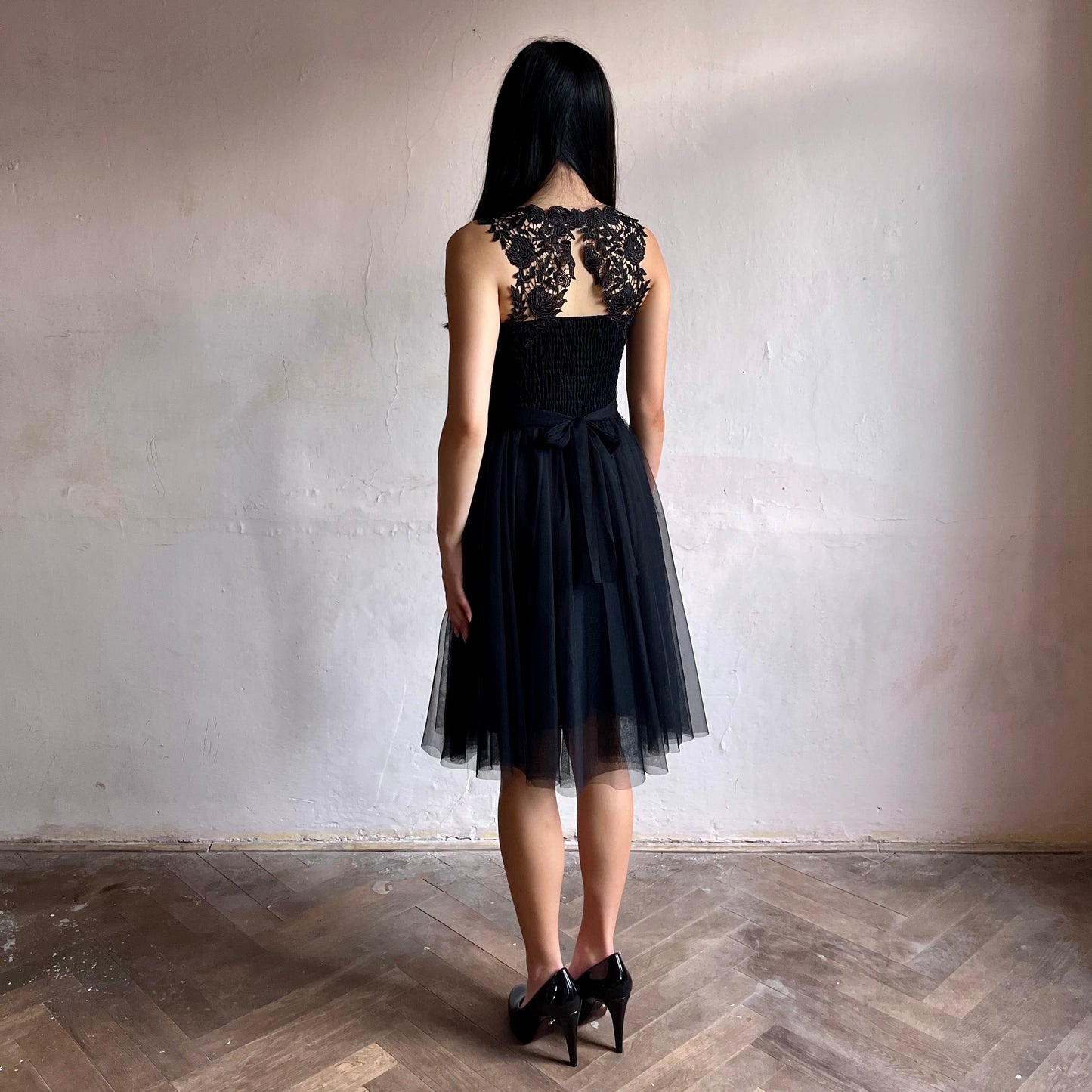 Modelka asijského původu pózující zezadu oblečená ve krátkých černých společenských šatech 