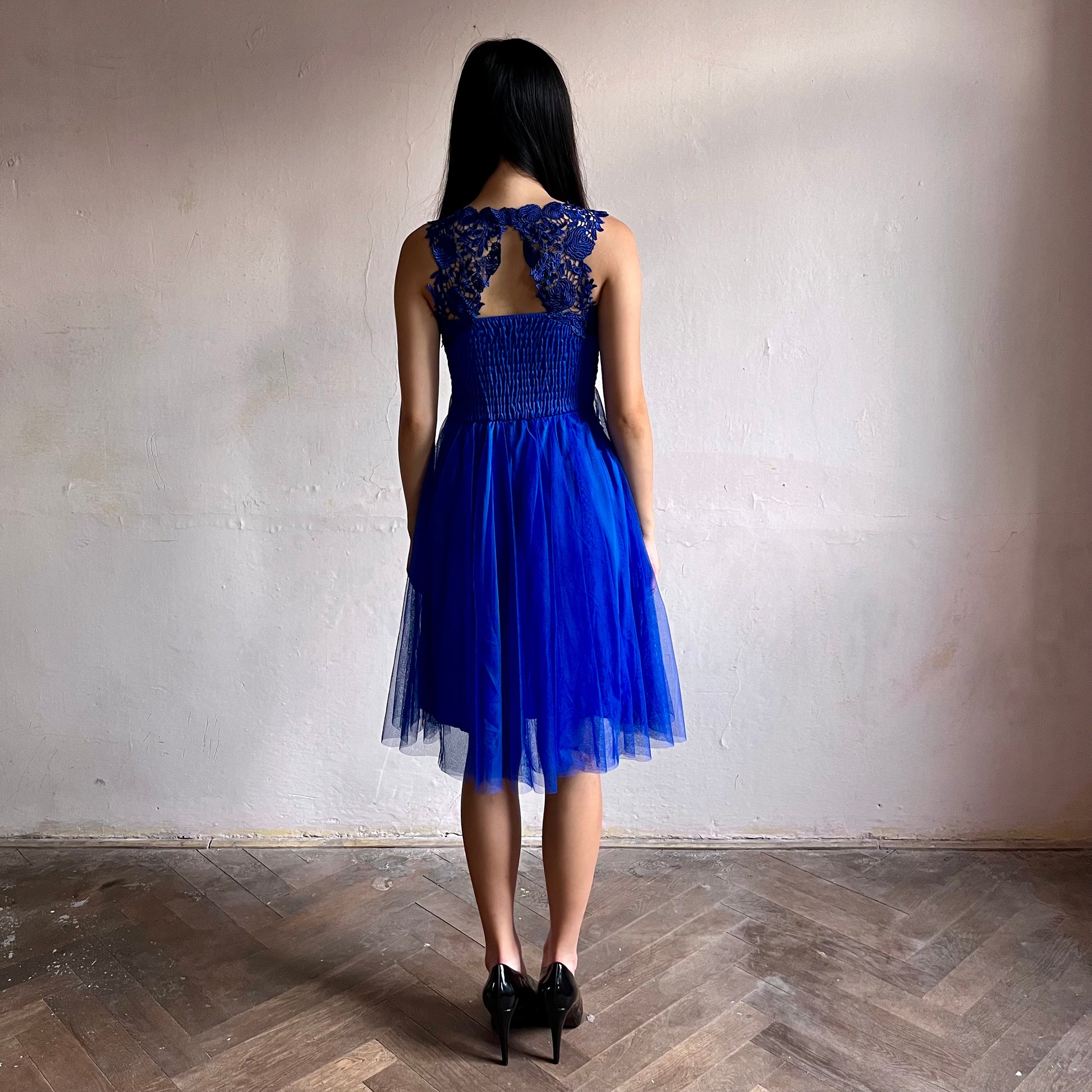 Modelka asijského původu pózující zezadu oblečená ve krátkých královsky modrých společenských šatech 