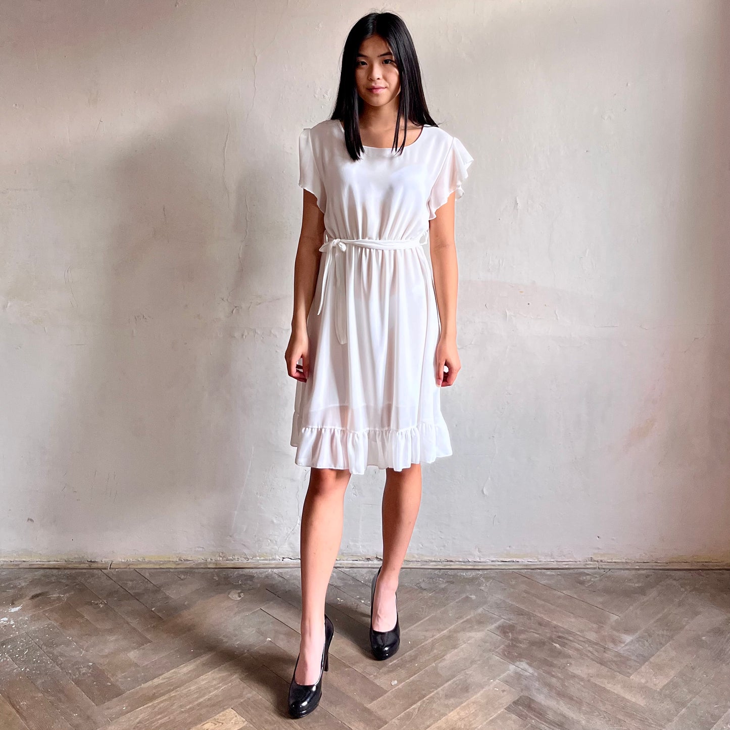 Modelka asijského původu pózující zepředu oblečená ve krátkých bílých společenských šatech s volány