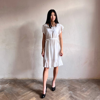 Modelka asijského původu pózující zepředu oblečená ve krátkých bílých společenských šatech s volány