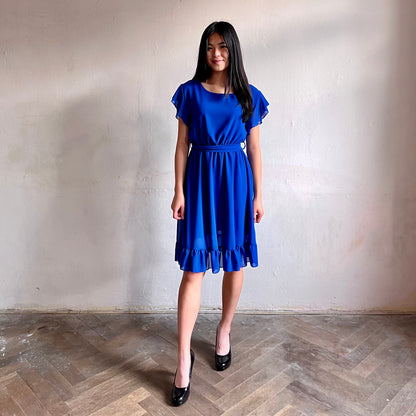 Modelka asijského původu pózující zepředu oblečená ve krátkých modrých společenských šatech s volány