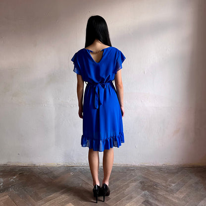Modelka asijského původu pózující zezadu oblečená ve krátkých modrých společenských šatech s volány