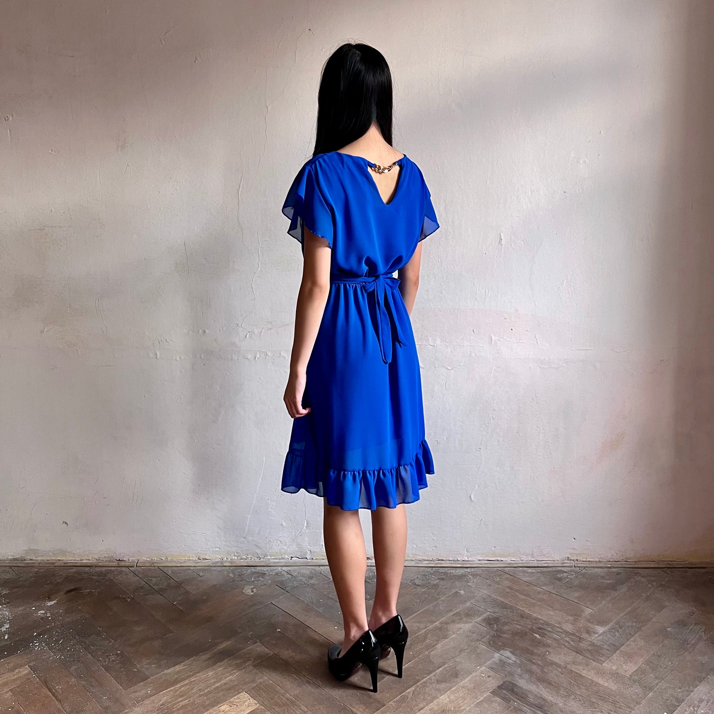 Modelka asijského původu pózující z boku oblečená ve krátkých modrých společenských šatech s volány