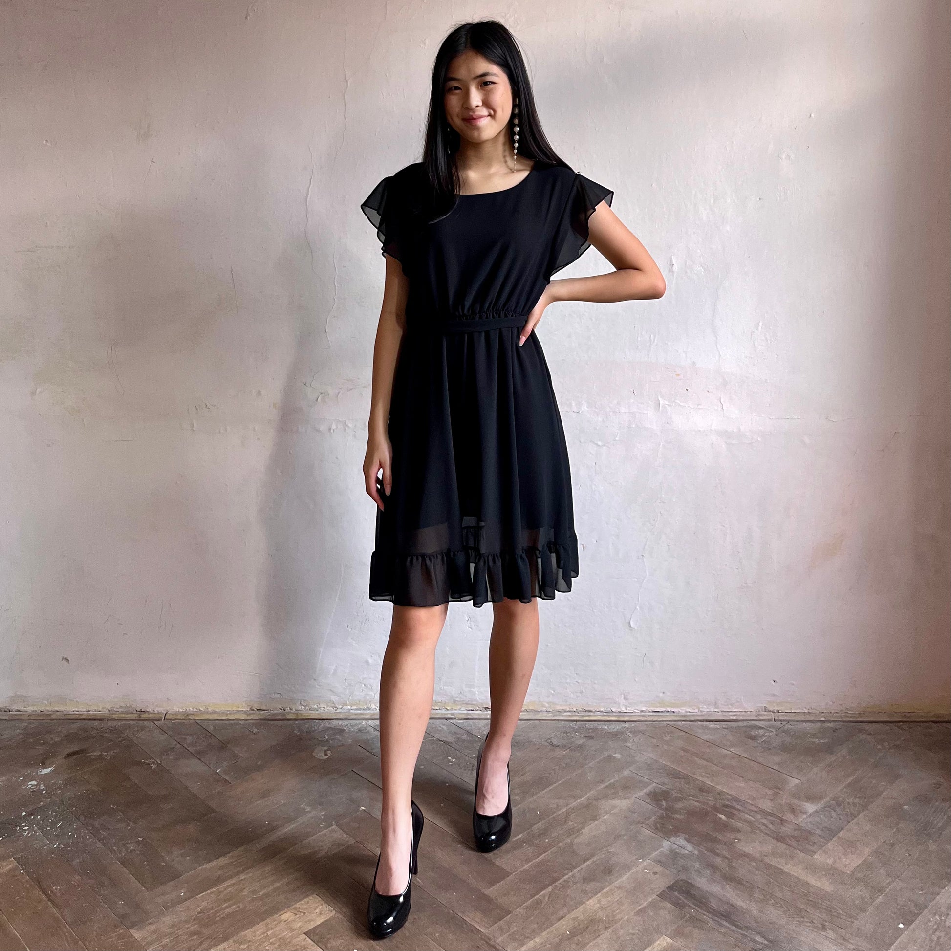 Modelka asijského původu pózující zepředu oblečená ve krátkých černých společenských šatech s volány