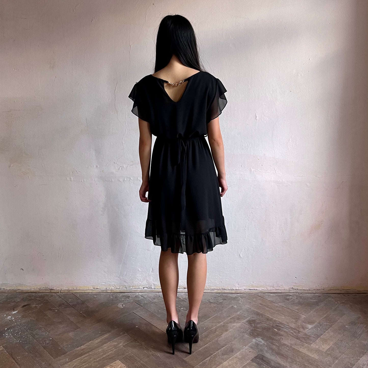 Modelka asijského původu pózující zezadu oblečená ve krátkých černých společenských šatech s volány