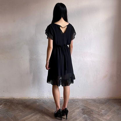 Modelka asijského původu pózující z boku oblečená ve krátkých černých společenských šatech s volány