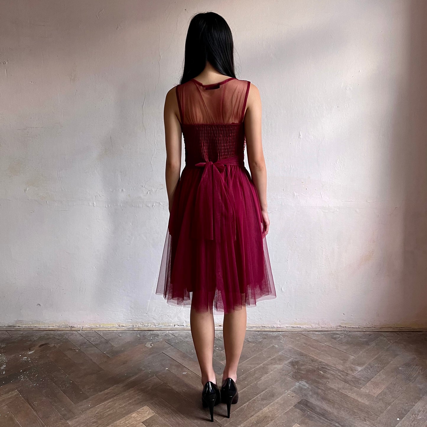 Modelka asijského původu pózující zezadu oblečená ve krátkých krajkovaných vínových společenských šatech