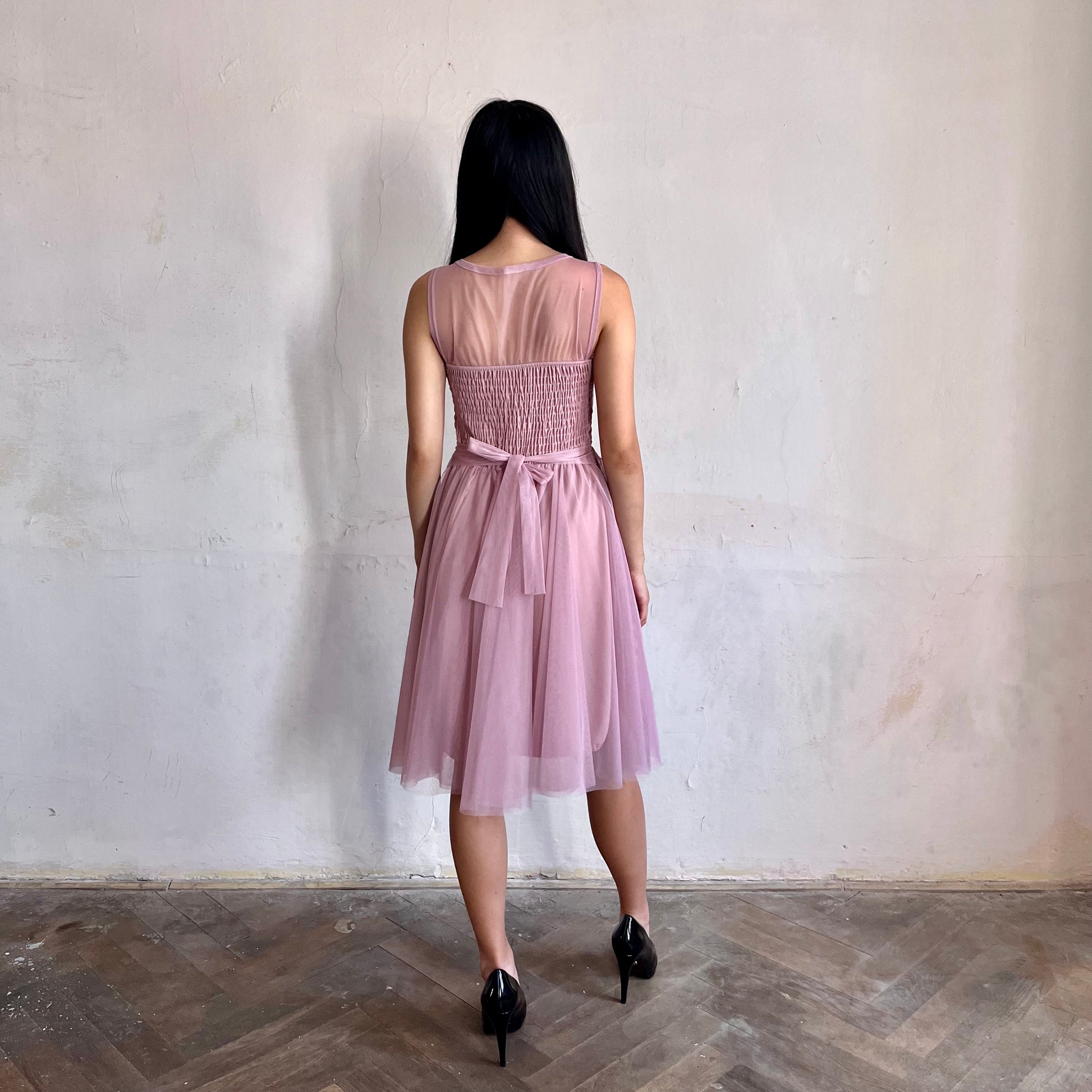 Modelka asijského původu pózující zezadu oblečená ve krátkých krajkovaných růžových společenských šatech