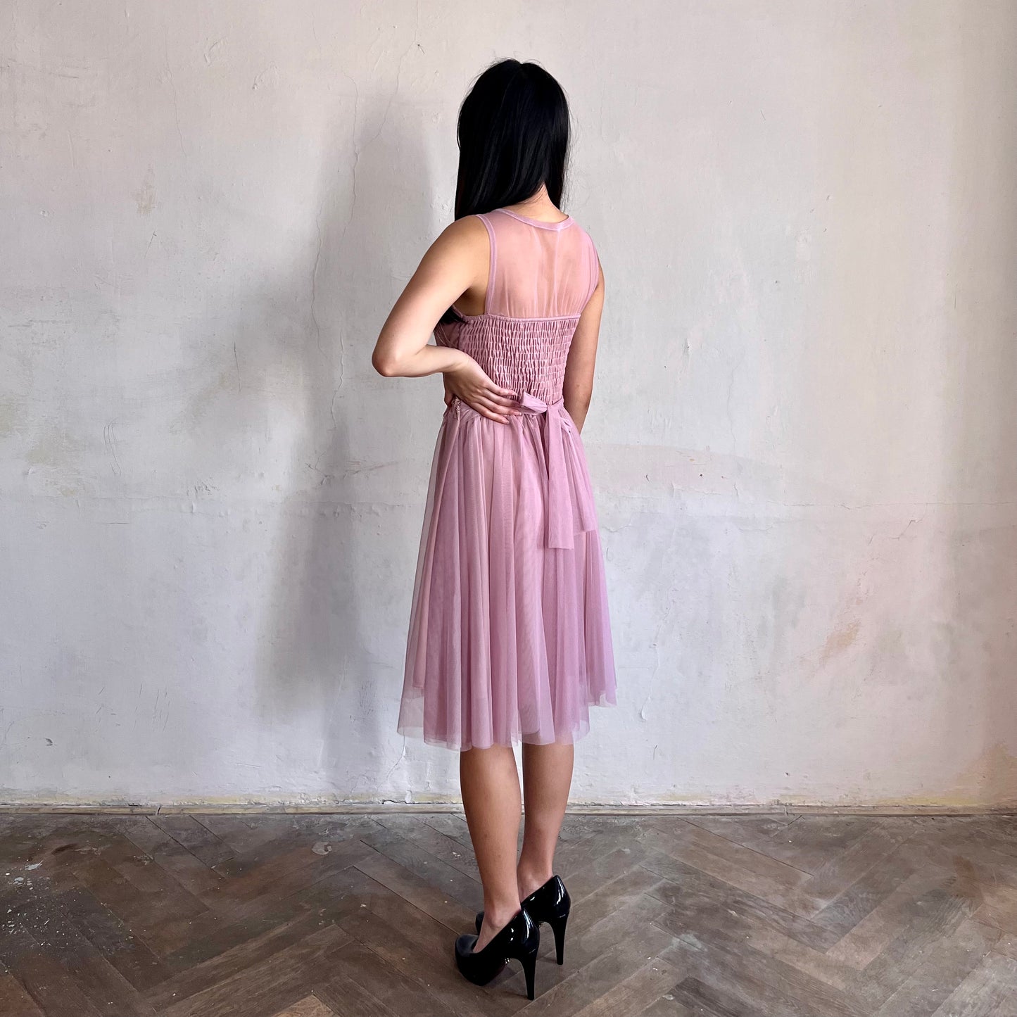 Modelka asijského původu pózující z boku oblečená ve krátkých krajkovaných růžových společenských šatech