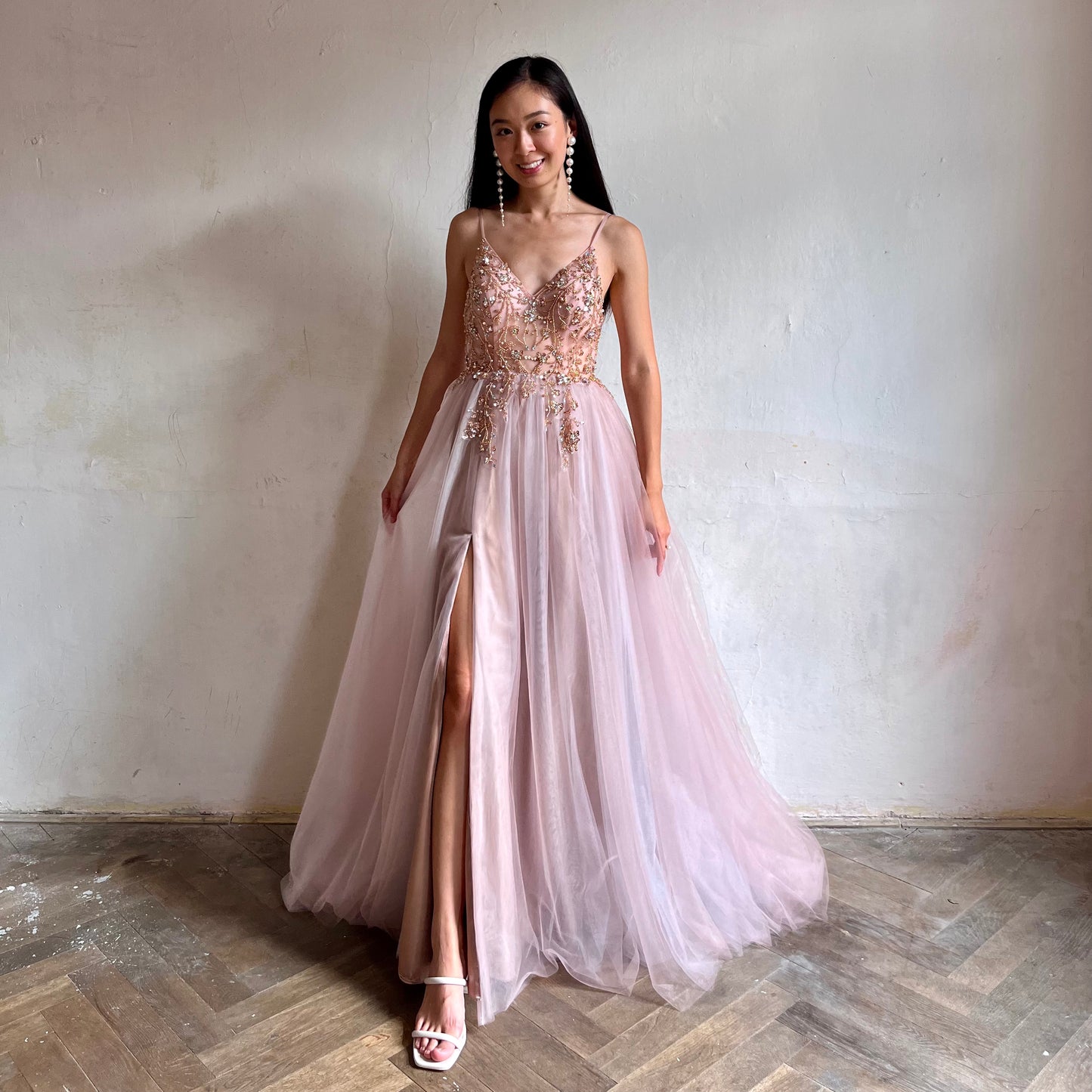 Modelka asijského původu pózující zepředu oblečená v dlouhých růžových plesových šatech s rozparkem 
