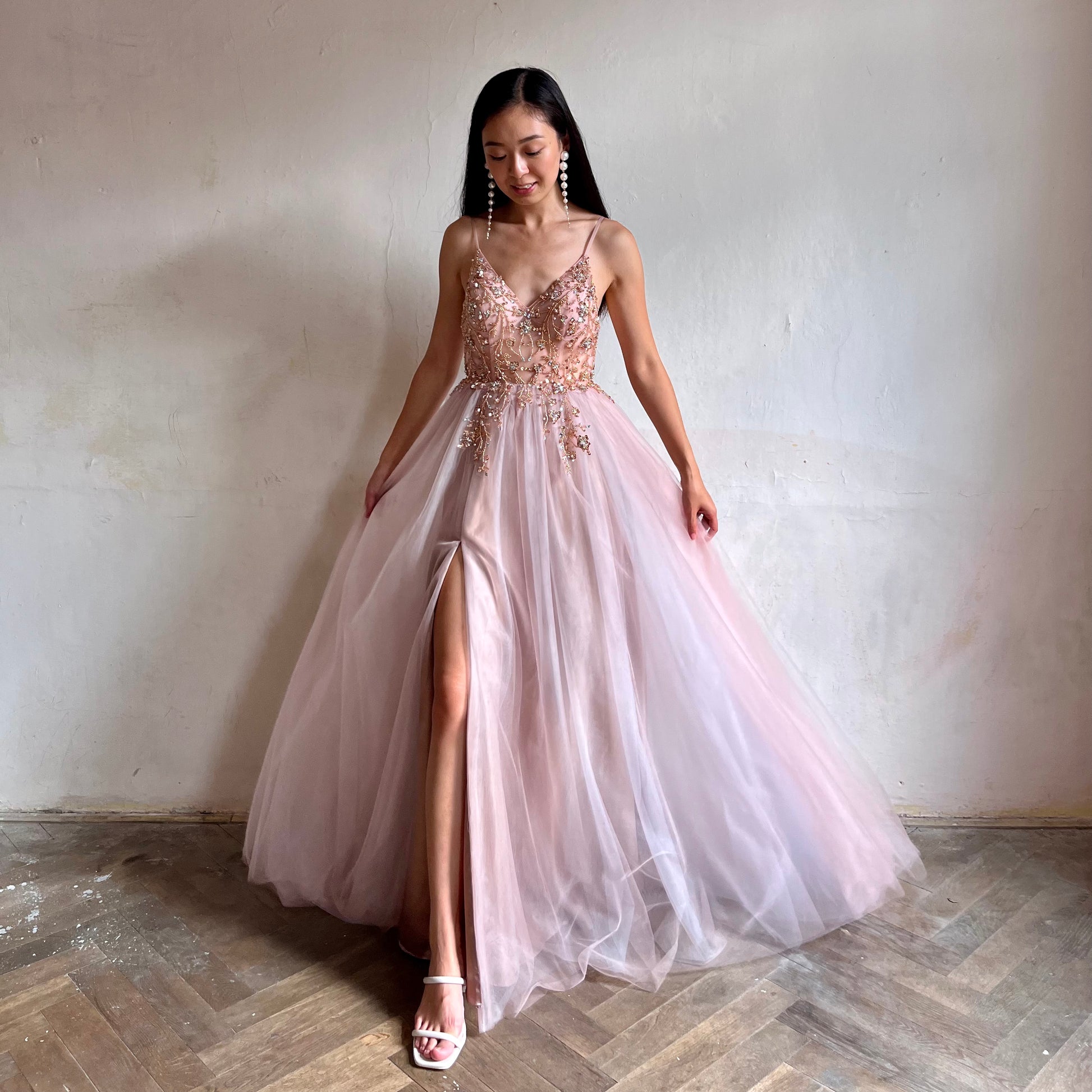 Modelka asijského původu pózující zepředu oblečená v dlouhých růžových plesových šatech s rozparkem 