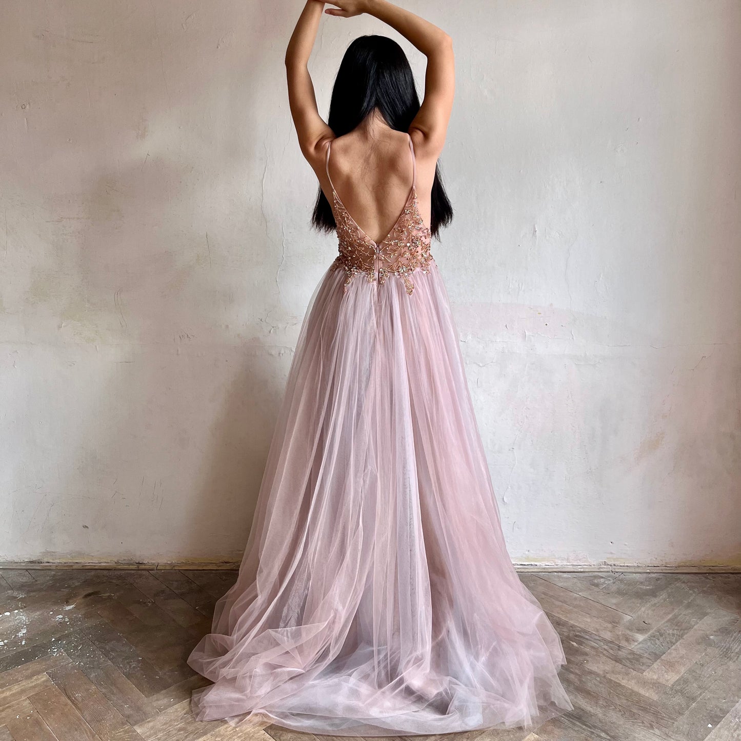Modelka asijského původu pózující zezadu oblečená v dlouhých růžových plesových šatech s rozparkem