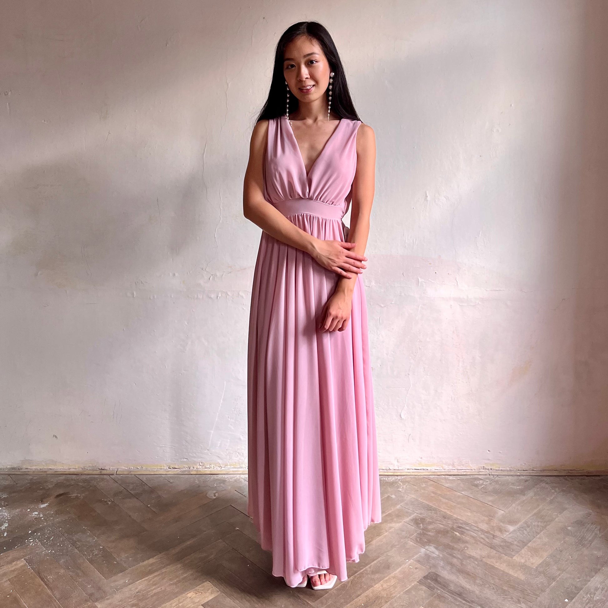 Modelka asijského původu pózující zepředu oblečená ve světle růžových společenských šatech