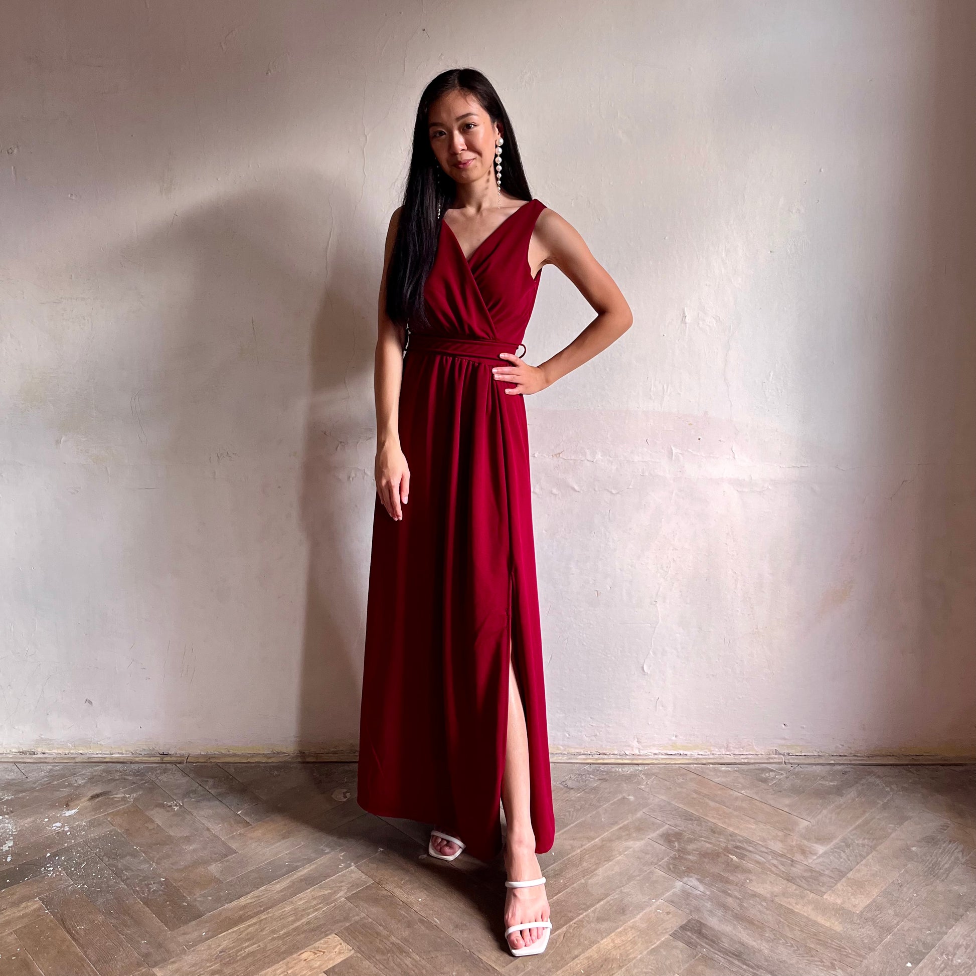Modelka asijského původu pózující zepředu oblečená ve vínových společenských šatech s rozparkem