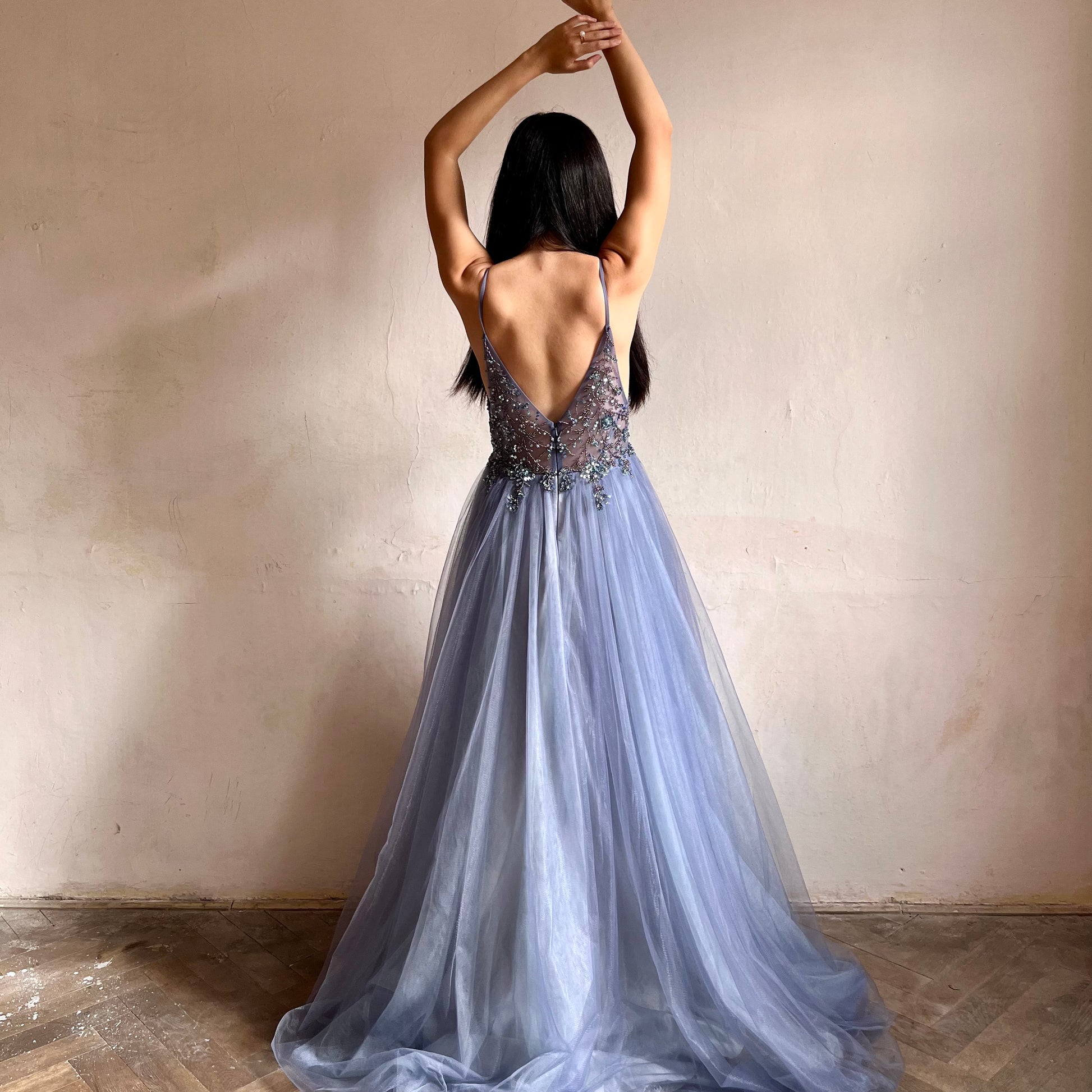 Modelka asijského původu pózující zezadu oblečená v dlouhých modrých plesových šatech s rozparkem 