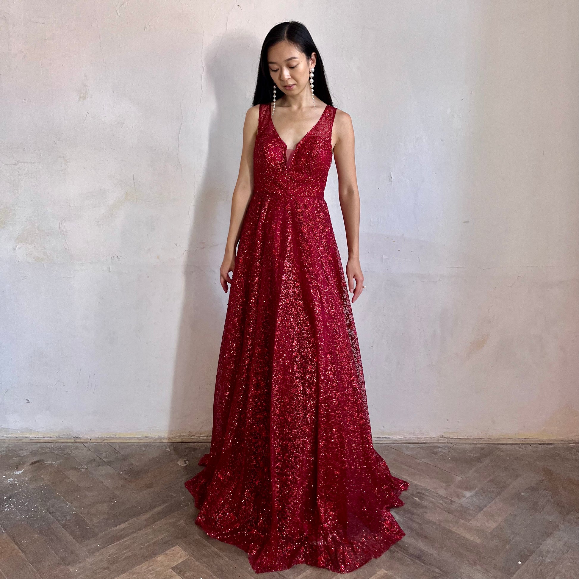 Modelka asijského původu pózující zepředu oblečená v červených třpytivých společenských šatech