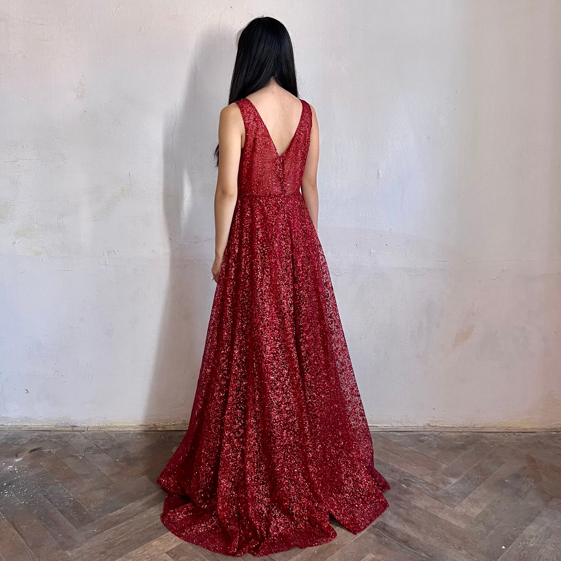 Modelka asijského původu pózující z boku oblečená v červených třpytivých společenských šatech