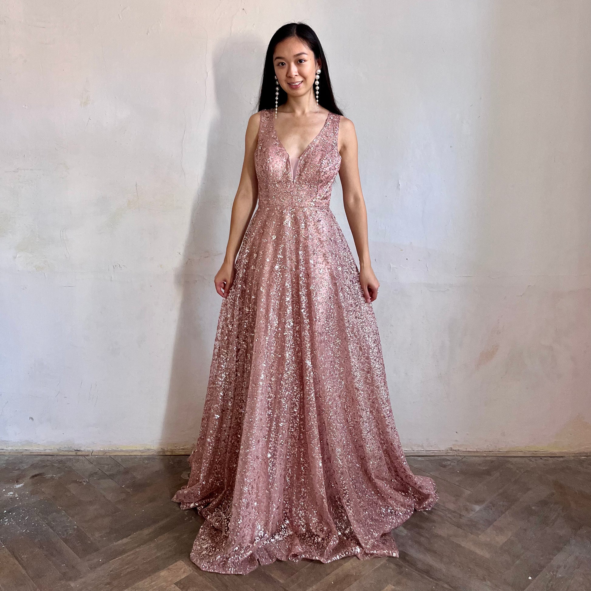 Modelka asijského původu pózující zepředu oblečená ve světle růžových třpytivých společenských šatech