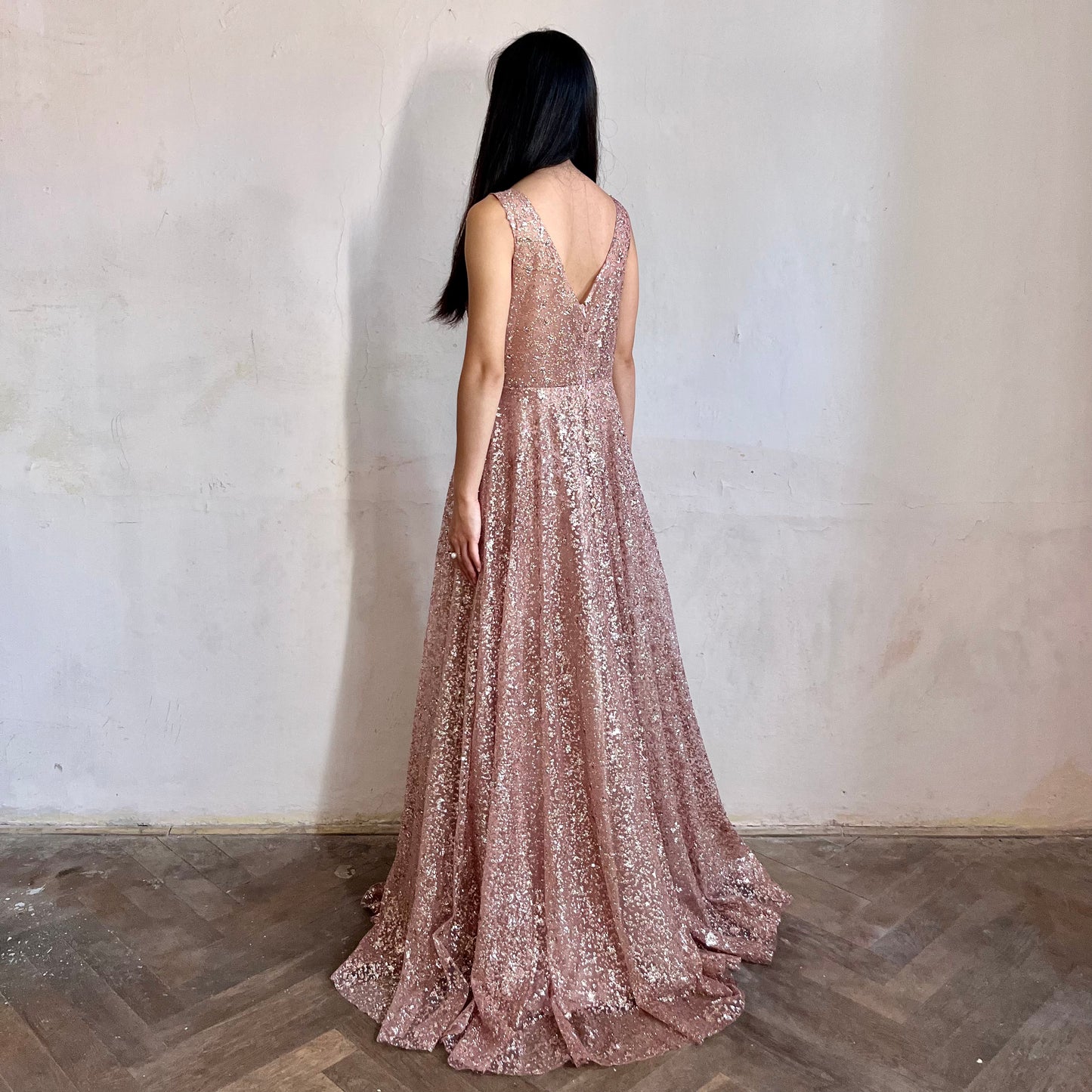 Modelka asijského původu pózující z boku oblečená ve světle růžových třpytivých společenských šatech