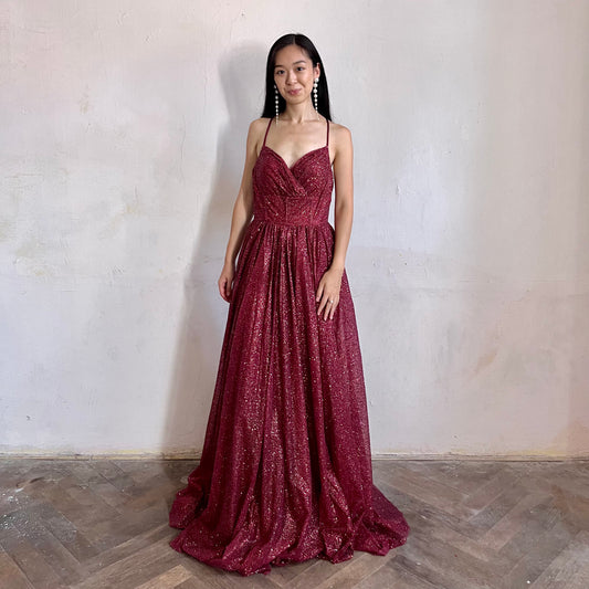 Modelka asijského původu pózující zepředu oblečená ve vínových třpytivých společenských šatech