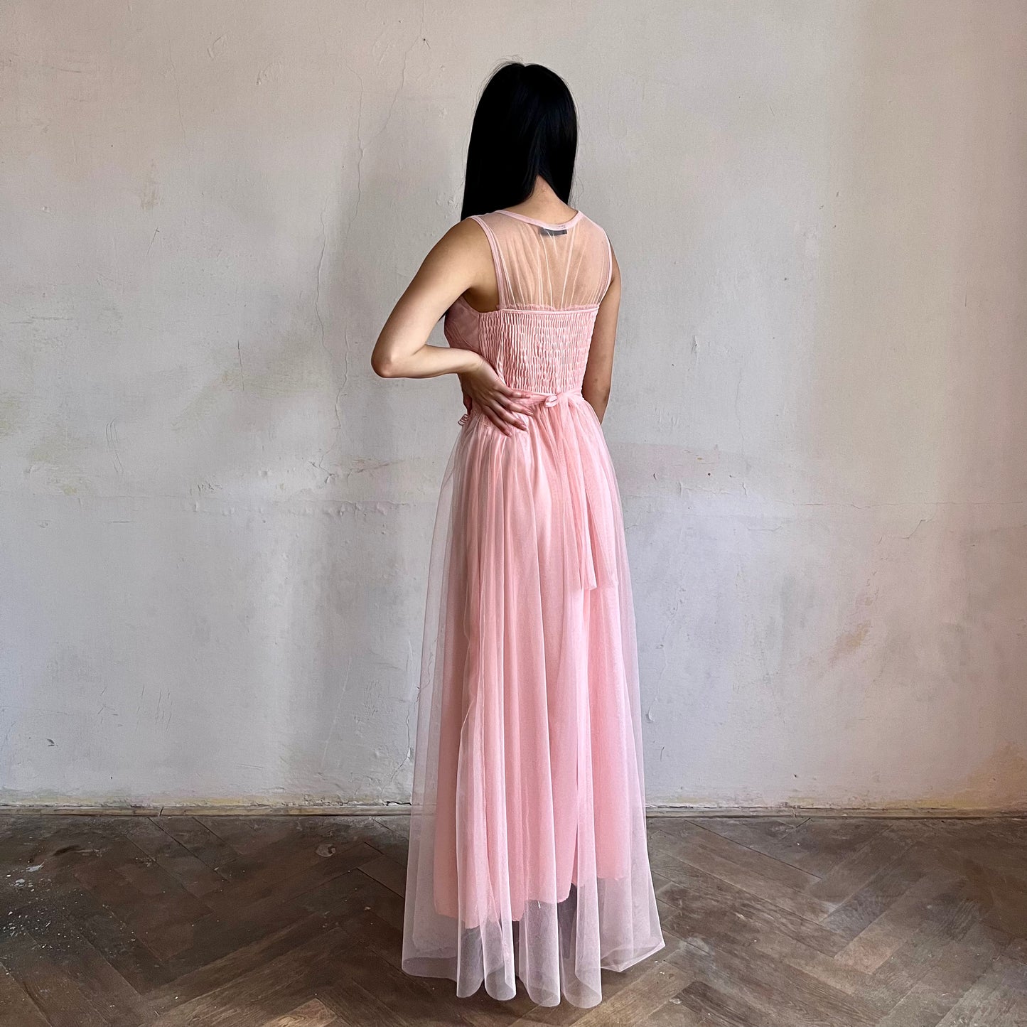 Modelka asijského původu pózující z boku oblečená ve světle růžových společenských šatech