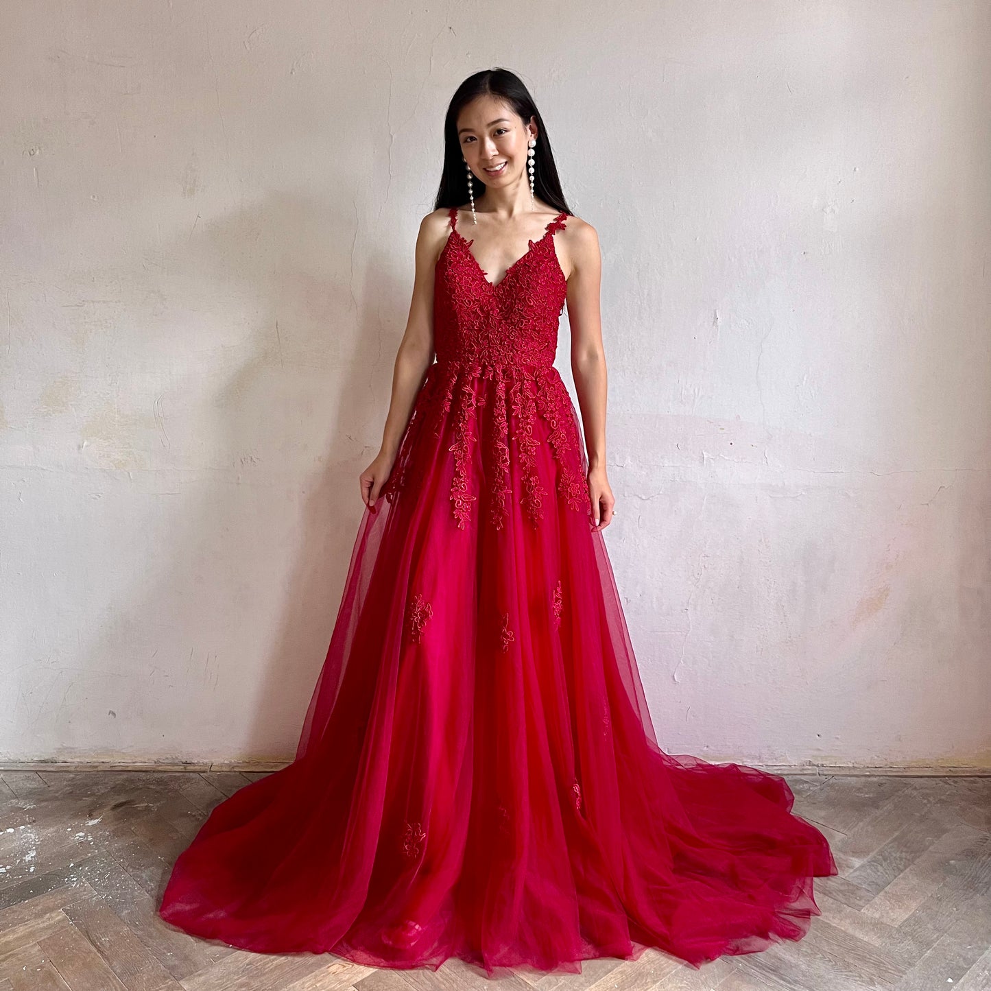 Modelka asijského původu pózující zepředu oblečená v dlouhých červených třpytivých plesových šatech 