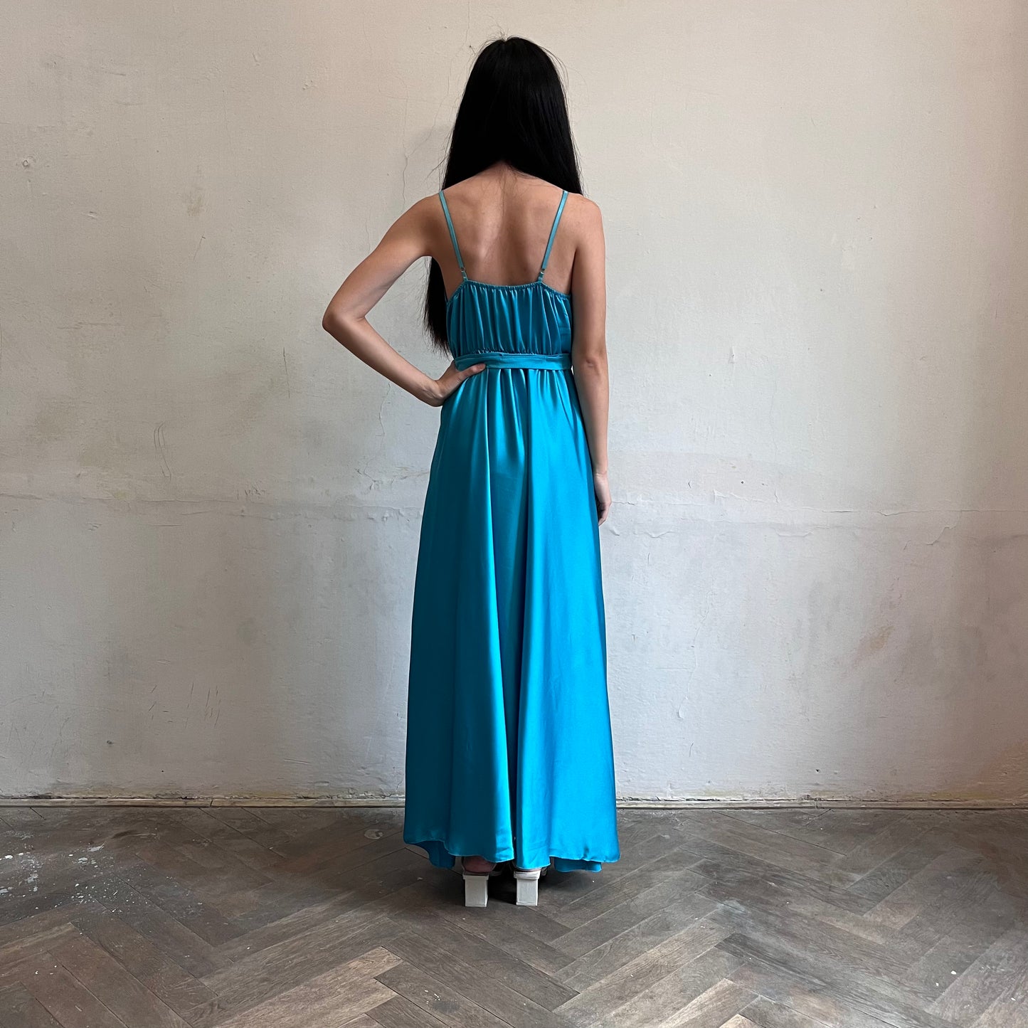 Modelka asijského původu pózující zezadu oblečená v tyrkysových společenských šatech s rozparkem