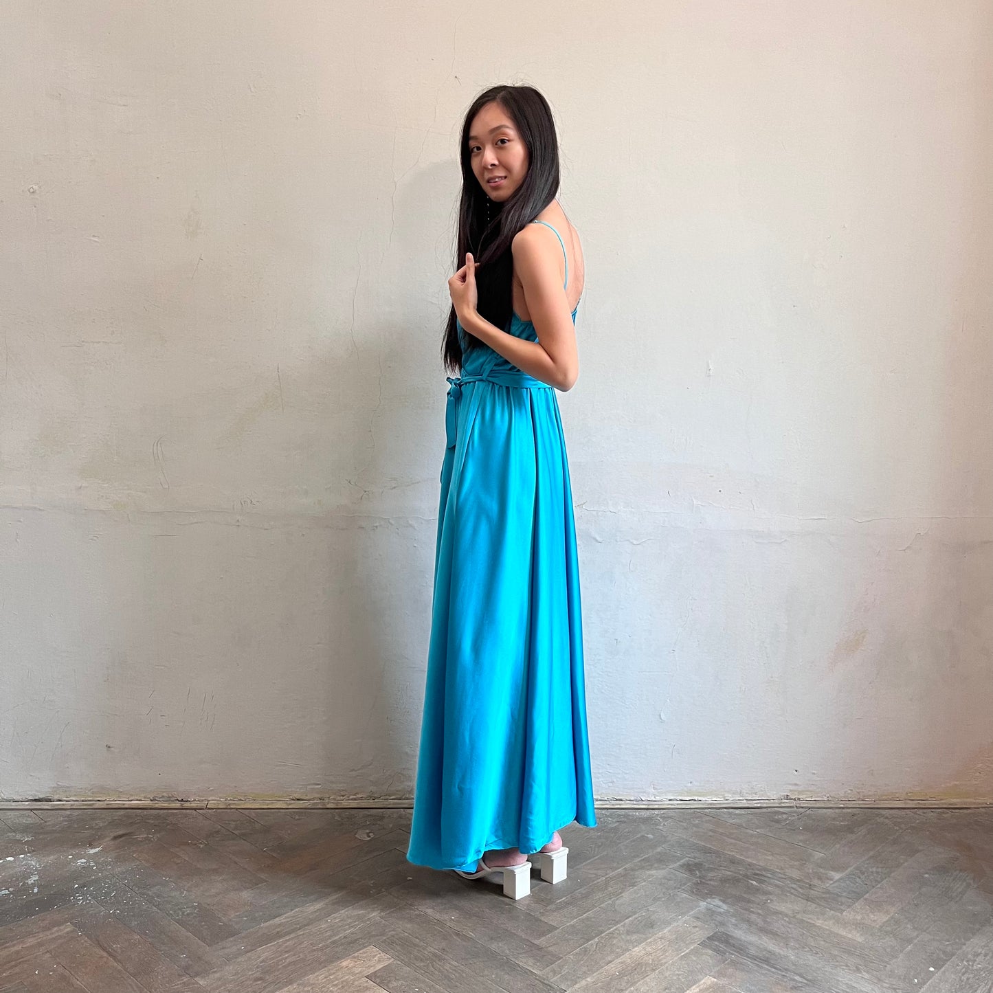 Modelka asijského původu pózující z boku oblečená v tyrkysových společenských šatech s rozparkem