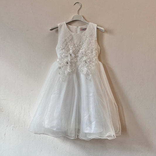 Dívčí bílé krajkované šaty visící na věšáku zadní stranou ke zdi