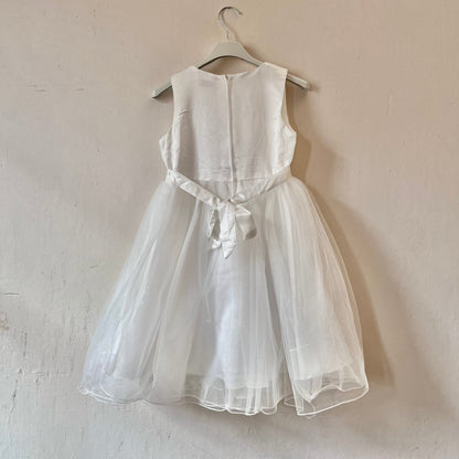Dívčí bílé krajkované šaty visící na věšáku přední stranou ke zdi