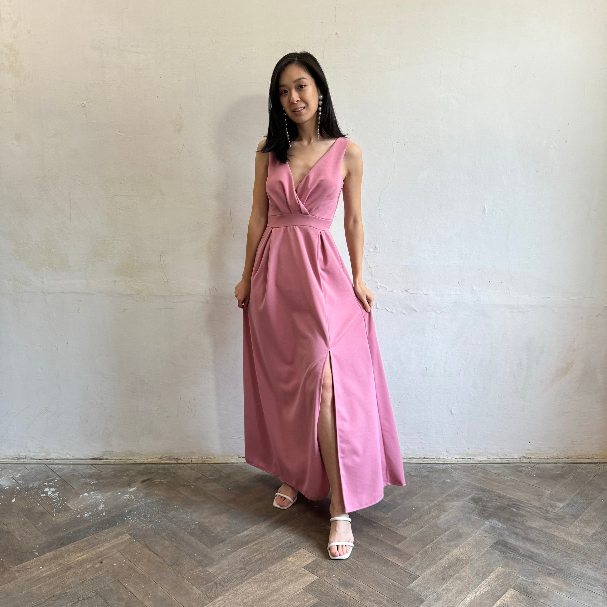 Modelka asijského původu pózující zepředu oblečená ve tmavě růžových společenských šatech s rozparkem