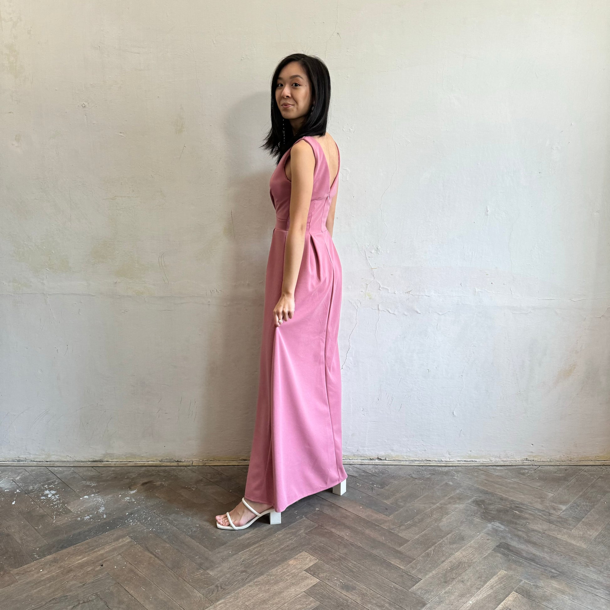 Modelka asijského původu pózující z boku oblečená ve tmavě růžových společenských šatech s rozparkem