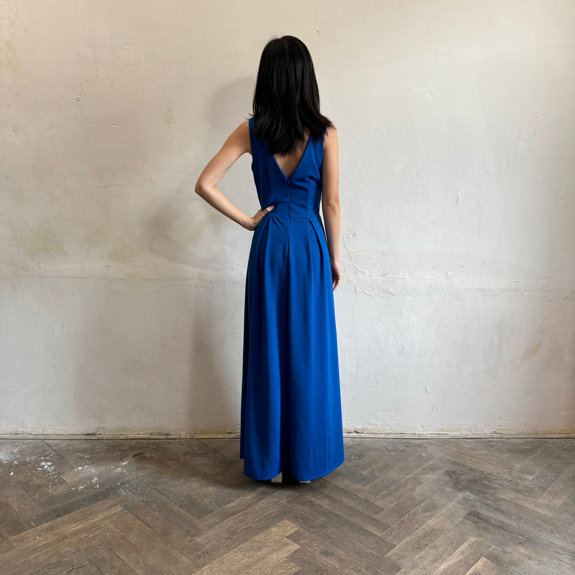 Modelka asijského původu pózující zezadu oblečená ve královsky modrých společenských šatech s rozparkem