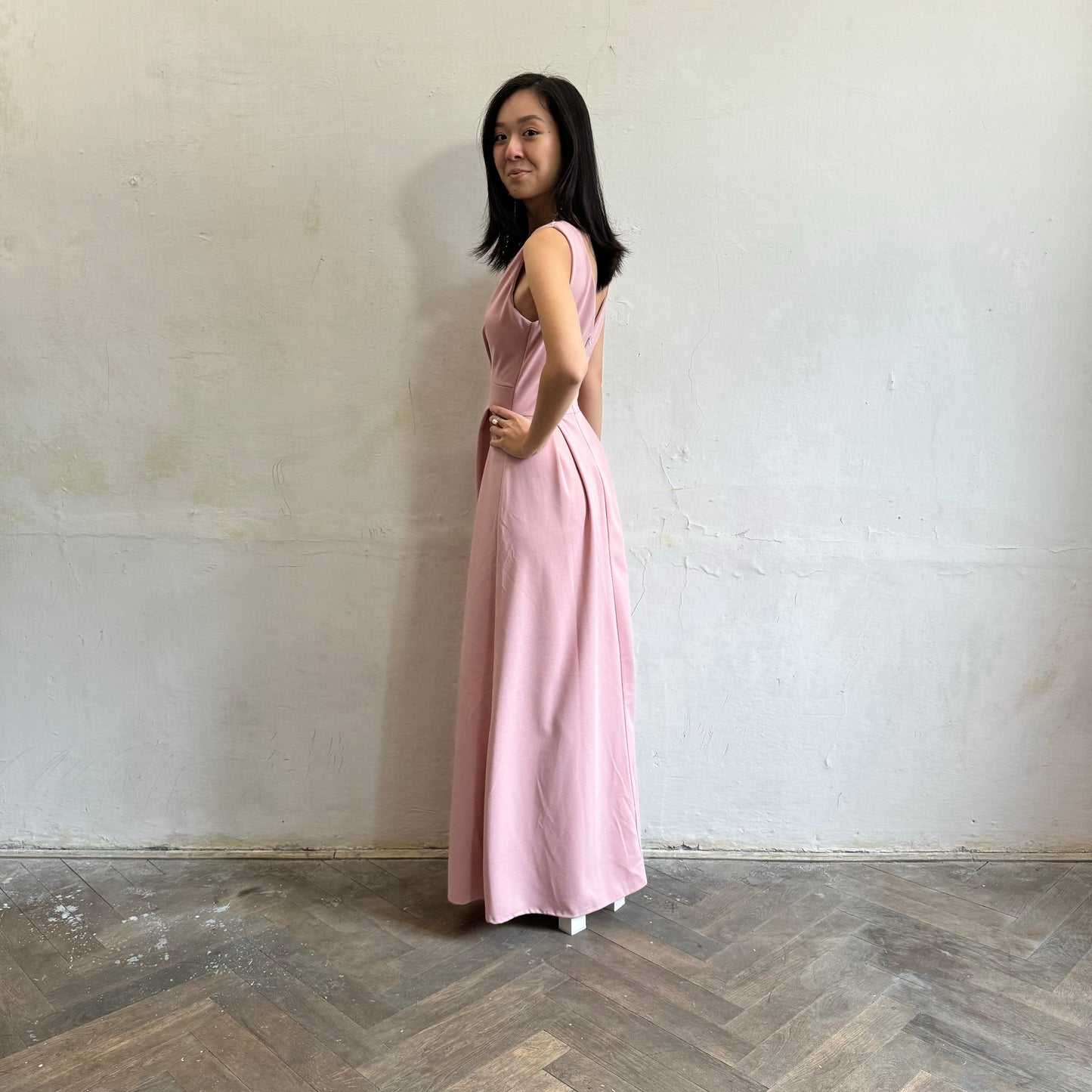 Modelka asijského původu pózující z boku oblečená ve světle růžových společenských šatech s rozparkem