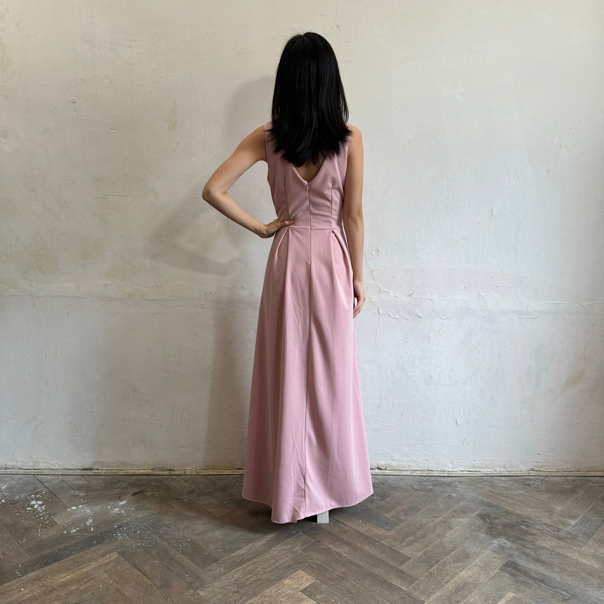 Modelka asijského původu pózující zezadu oblečená ve světle růžových společenských šatech s rozparkem