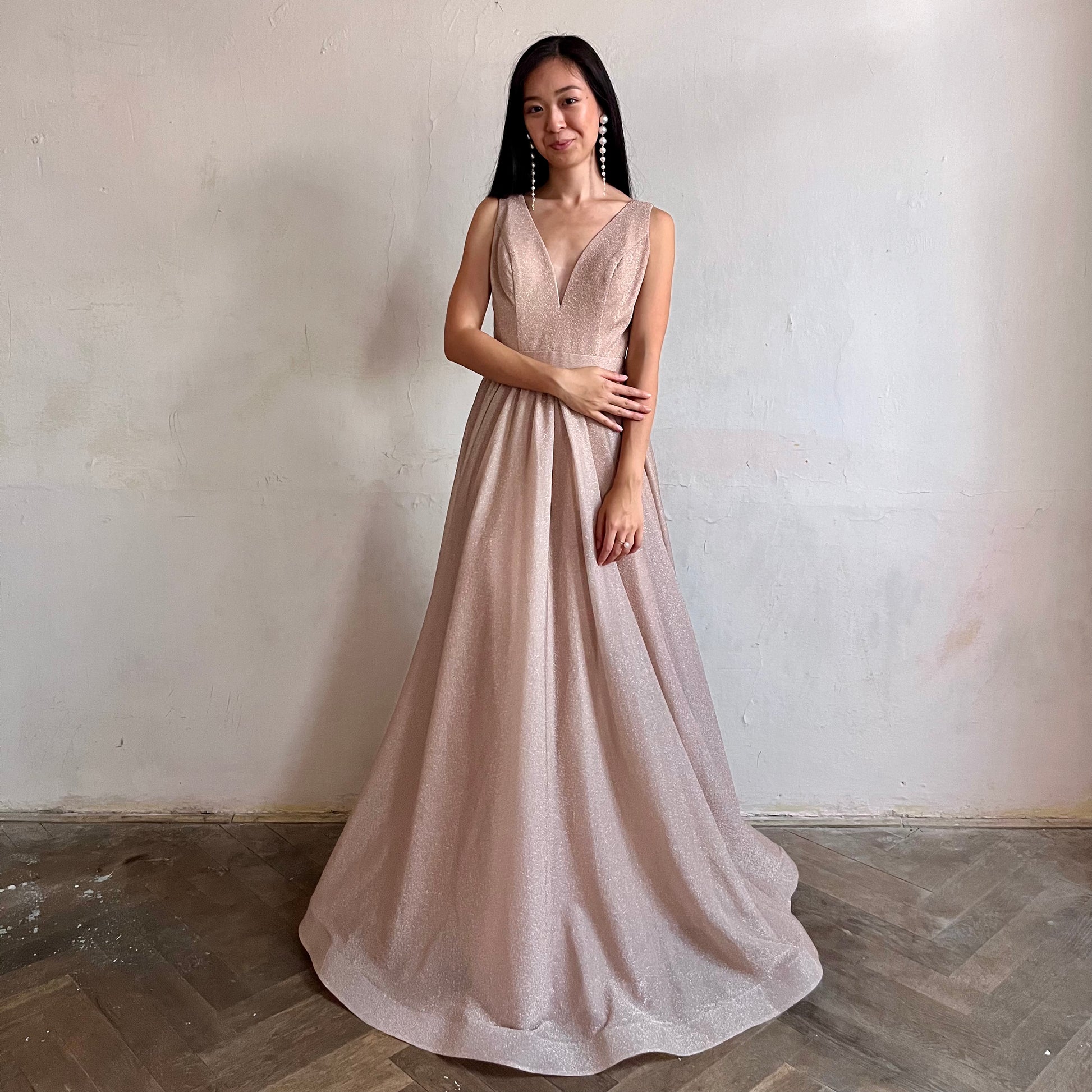 Modelka asijského původu pózující zepředu oblečená v dlouhých světle růžových třpytivých společenských šatech 