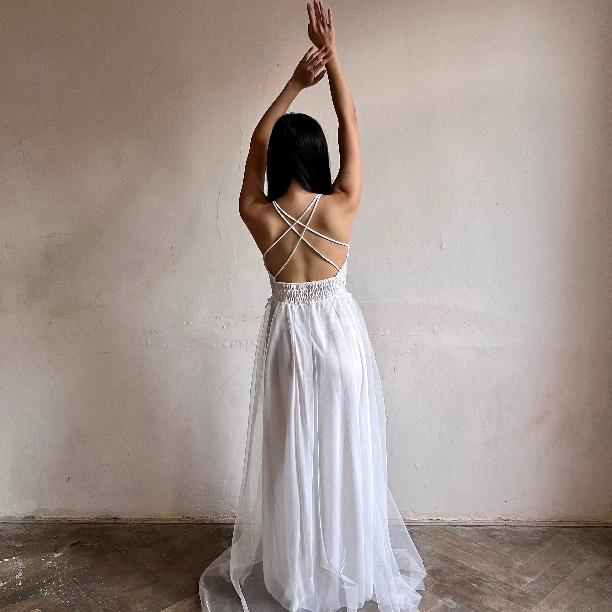 Modelka asijského původu pózující zezadu oblečená v dlouhých bílých společenských šatech 
