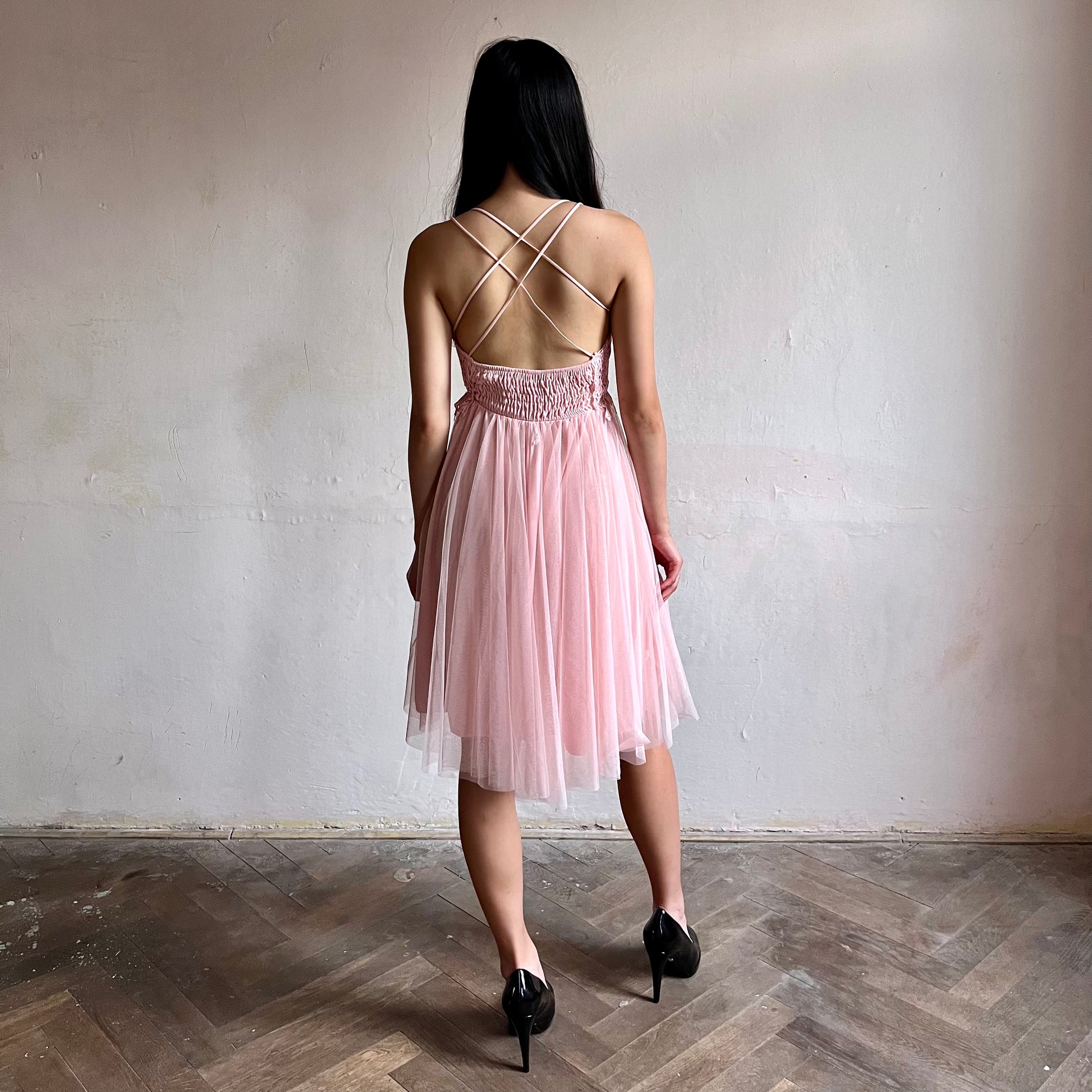 Modelka asijského původu pózující zezadu oblečená v krátkých světle růžových společenských šatech 