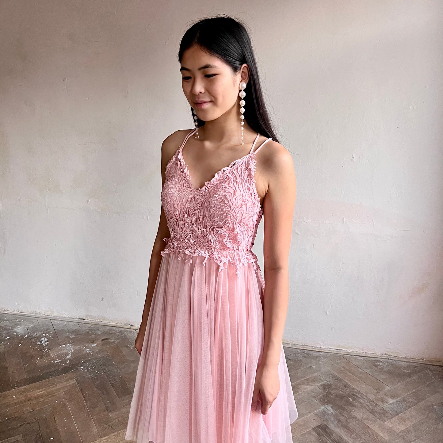 Modelka asijského původu pózující zepředu oblečená v krátkých světle růžových společenských šatech 