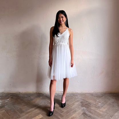 Modelka asijského původu pózující zepředu oblečená ve krátkých bílých společenských šatech 