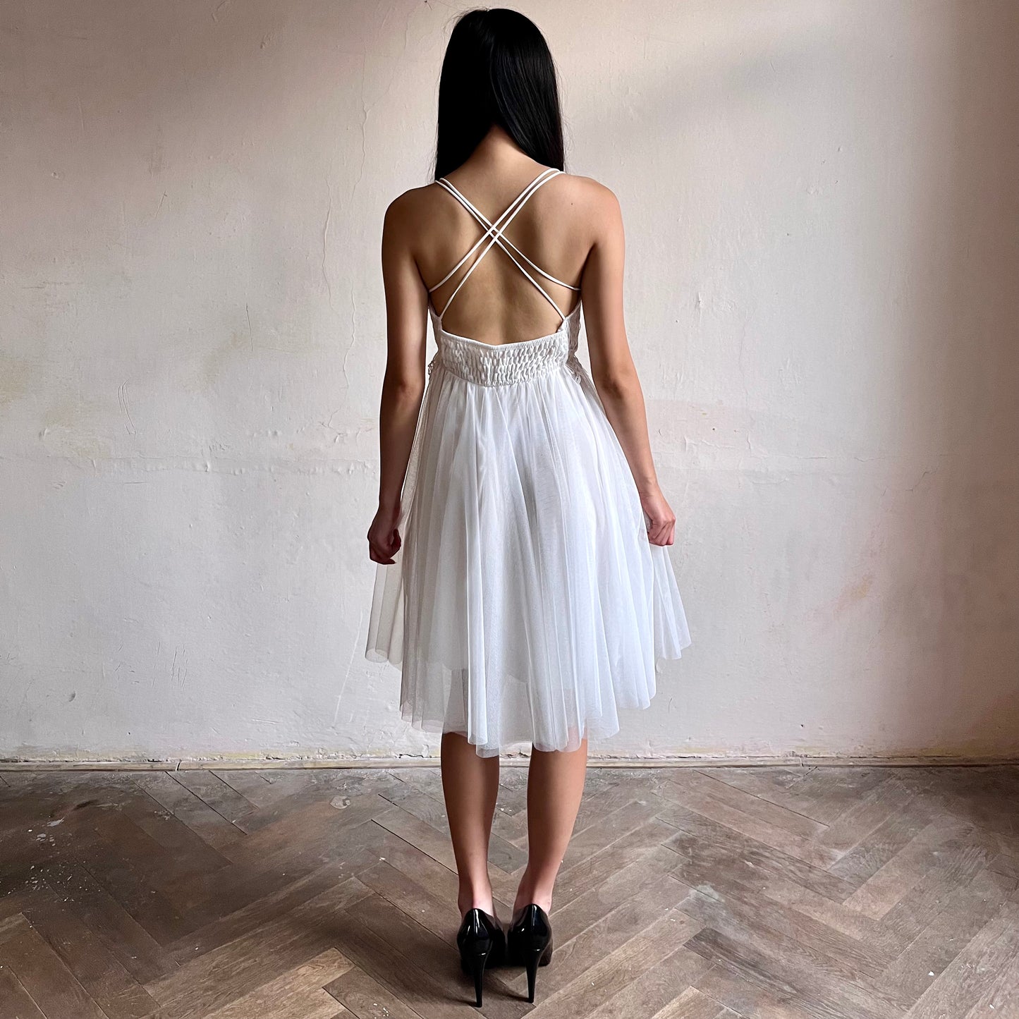 Modelka asijského původu pózující zezadu oblečená ve krátkých bílých společenských šatech 