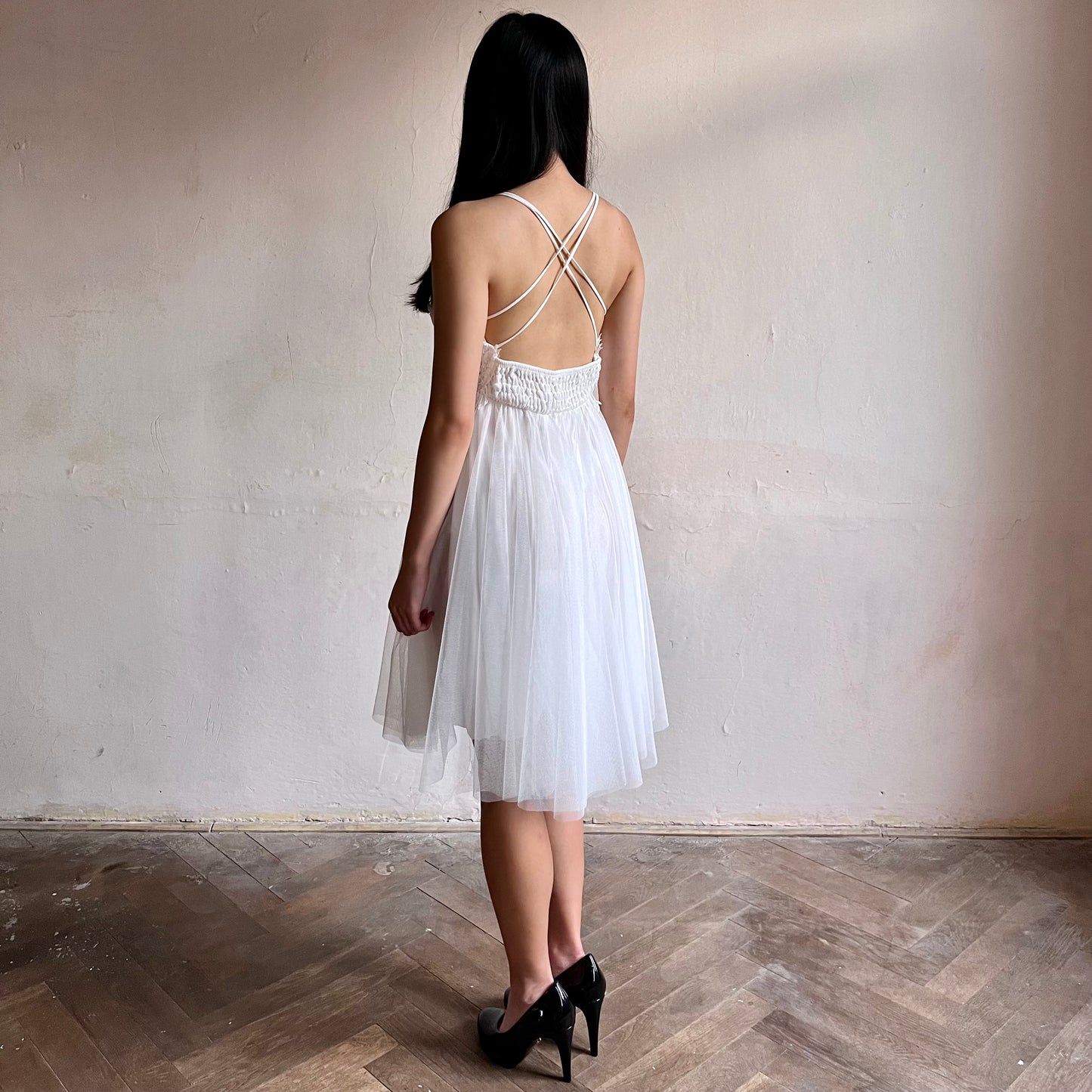 Modelka asijského původu pózující z boku oblečená ve krátkých bílých společenských šatech 