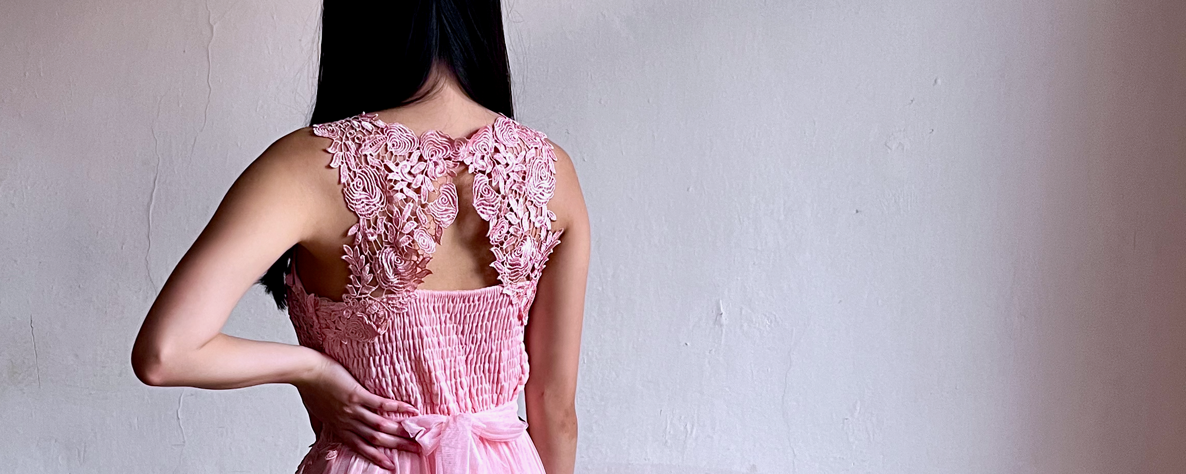 Pohled na modelku zezadu, která je oblečená v růžových šatech s krajkovaným detailem